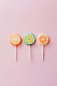 Three fruity lollipops arranged on a pink background, offering vibrant citrus hues.